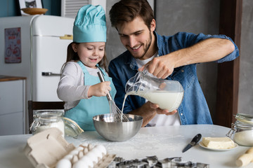 Daddy with daughter baking cake together in home kitchen.