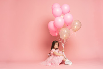 Happy celebration of birthday party with flying balloons of charming cute little girl in tulle dress smiling to camera isolated on pink background. Charming smile, expressing happiness