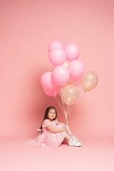 Happy celebration of birthday party with flying balloons of charming cute little girl in tulle dress smiling to camera isolated on pink background. Charming smile, expressing happiness