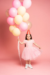 Obraz na płótnie Canvas Happy celebration of birthday party with flying balloons of charming cute little girl in tulle dress smiling to camera isolated on pink background. Charming smile, expressing happiness
