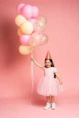 Obraz na płótnie Canvas Happy celebration of birthday party with flying balloons of charming cute little girl in tulle dress smiling to camera isolated on pink background. Charming smile, expressing happiness