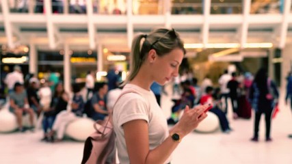Caucasian hipster girl with backpack searching information about shopping center on content website while walking around public place with cellular phone in hands - Powered by Adobe