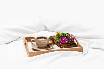 Fresh morning coffee with wrapped flowers on a board on a bed sheet 