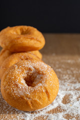 Top view of donuts with selective focus on wooden board and sugar with black background in vertical