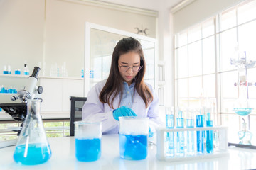 In a modern laboratory, a female chemist conducts experiments on the synthesis of compounds using a dropper and a solution in a test tube. COVID-19