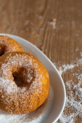 Top view of two donuts in plate with sugar on wooden board and sugar in vertical