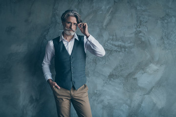 Portrait of pensive minded elegant rich wealthy old macho man touch his modern spectacles put hands pocket wear good look brown pants trousers isolated over grey color background