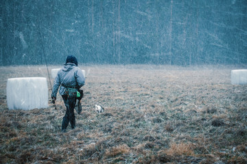 A fisherman with a fishing rod in his hands during a snowfall.