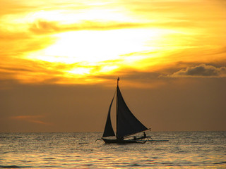 Fototapeta na wymiar SILHOUETTE: Local Filipino person sails along a calm ocean at golden sunset.