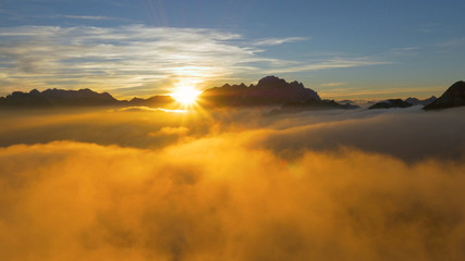 DRONE: Flying over clouds and a rocky ridge high in the French Alps at sunrise.