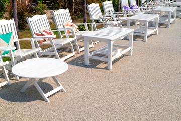 A white wooden armchair and table row beside the pool