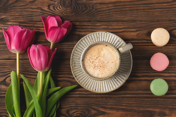 pink tulips, cup with coffee and macaroon cookies on a wooden background, copy space