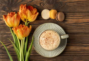 orange tulips, cup with coffee and macaroon cookies on a wooden background, copy space