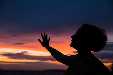 Dark silhouette of a woman on a background of a beautiful sunset sky. Ocean, sunset, man’s power.