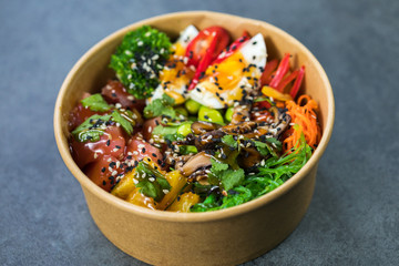 Poke bowl with salmon, guinoa, vegetables, friut and tofu on dark background