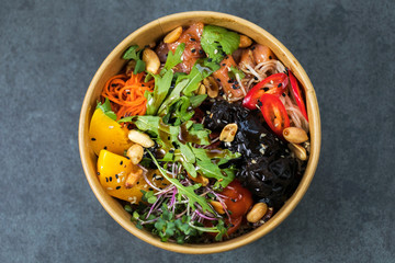 Poke bowl with salmon, guinoa, vegetables, friut and tofu on dark background