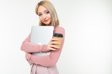 Naklejka premium girl in pink stylish clothes and blond hair holding a cup of coffee and a laptop in her hands on a white studio background with copy space