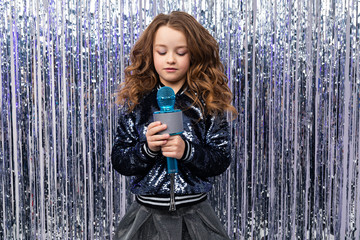 stylish girl with a microphone in her hands on a shiny tinsel background