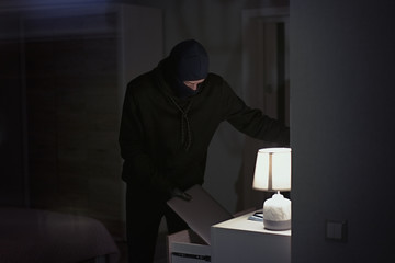 Burglar stealing and putting stolen laptop in bag  inside the house at night