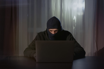 Male hacker in the hood in a dark room using computer virus program for cyber attack. Hackers and...