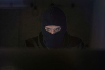 Male hacker in the hood in a dark room using computer virus program for cyber attack. Hackers and...