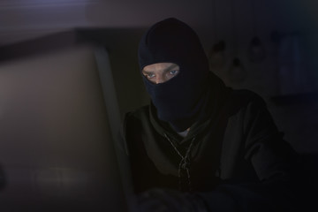 Male hacker in the hood in a dark room using computer virus program for cyber attack. Hackers and cyber security concept                               