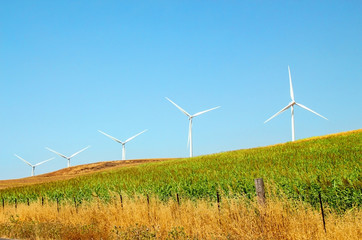 Windmills wind turbines farm power generators against landscape against blue sky in beautiful...
