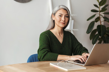Photo of gray-haired focused businesswoman typing on laptop