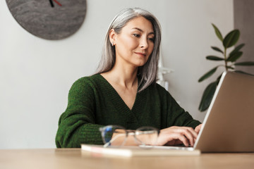 Photo of gray-haired focused businesswoman typing on laptop - Powered by Adobe