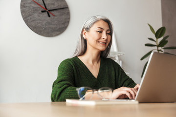 Photo of gray-haired smiling businesswoman typing on laptop