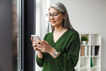 Photo of gray-haired pleased businesswoman using cellphone