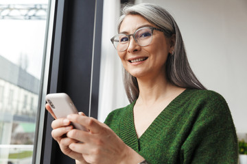 Photo of gray-haired joyful businesswoman using cellphone