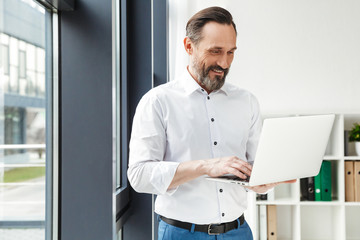 Fototapeta premium Photo of bearded smiling businessman in white shirt typing on laptop
