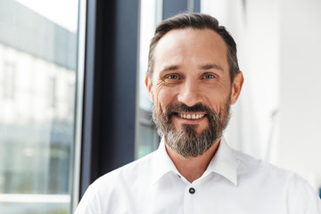 Photo of bearded pleased businessman smiling and looking at camera