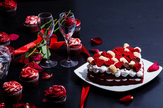 Layered Red Velvet Cake And Cupcakes In The Background With Two Champagne Glasses