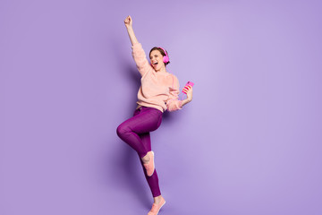 Full length photo of pretty lady hold telephone modern earphones on ears listen youth music dance students party wear casual stylish pink jumper pants isolated purple color background