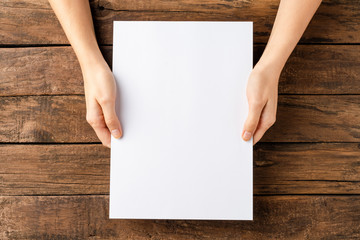 Young female hands holding paper sheet with copyspace. Top view