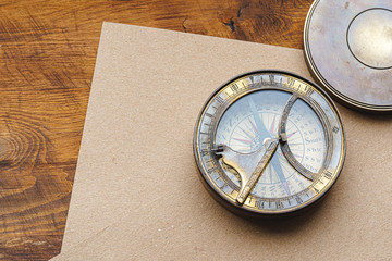 Vintage metal compass on carton paper on wooden table close up