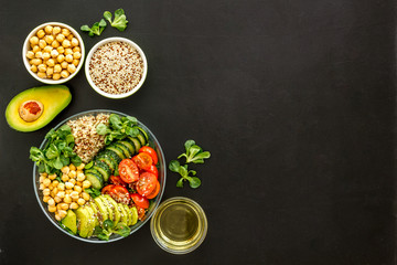 Healhty vegan lunch bowl. Avocado, quinoa, sweet potato, tomato, spinach and chickpeas vegetables salad on black table. Top view