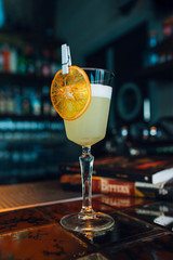 Pisco Sour cocktail with dried orange slice at bar or restaurant background. Closeup.