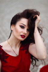 Portrait of a young brunette woman in a red dress with a train