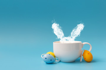 Steam in rabbit ears shape from coffee cup decorated easter colored eggs. Morning drink. Easter...