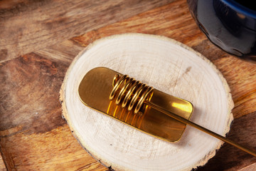 Gold honey spoon on wooden plank close up. Kitchen utensil