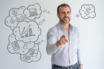 Latin man pointing to camera with hand drawn business sketches. Positive successful handsome guy on background with icons. Cheerful confident headhunter choosing you. Human resources concept