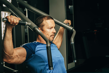 Fototapeta na wymiar Senior man doing exercises for arms in a training machine in gym