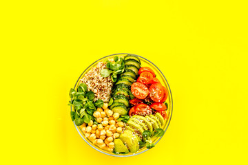 Healhty vegan lunch bowl. Avocado, quinoa, sweet potato, tomato, spinach and chickpeas vegetables salad on yellow table. Top view