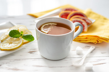 cup of black tea with lemon and grapefruit , close up on the white wooden background