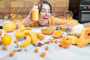 Portrait of a young and joyful woman holding bottle of juice at the table full of healthy raw vegetables and fruits. Concept of vegetarianism, detox, healthy eating and wellness