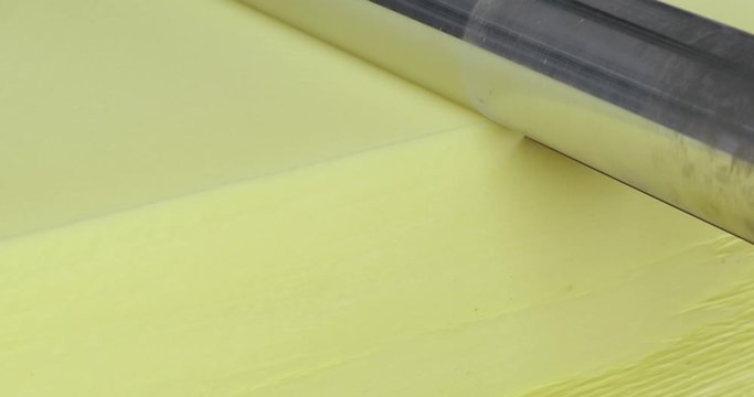 Close-up, a large yellow cube of foam passes through a wide sharp knife. production of soft products for domestic and industrial use. polyurethane foam lightweight material