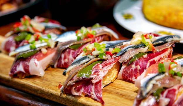 Appetizing spanish tapas with jamon, anchovies and green vegetables on wooden tray closeup in San Sebastian, Donostia, Spain